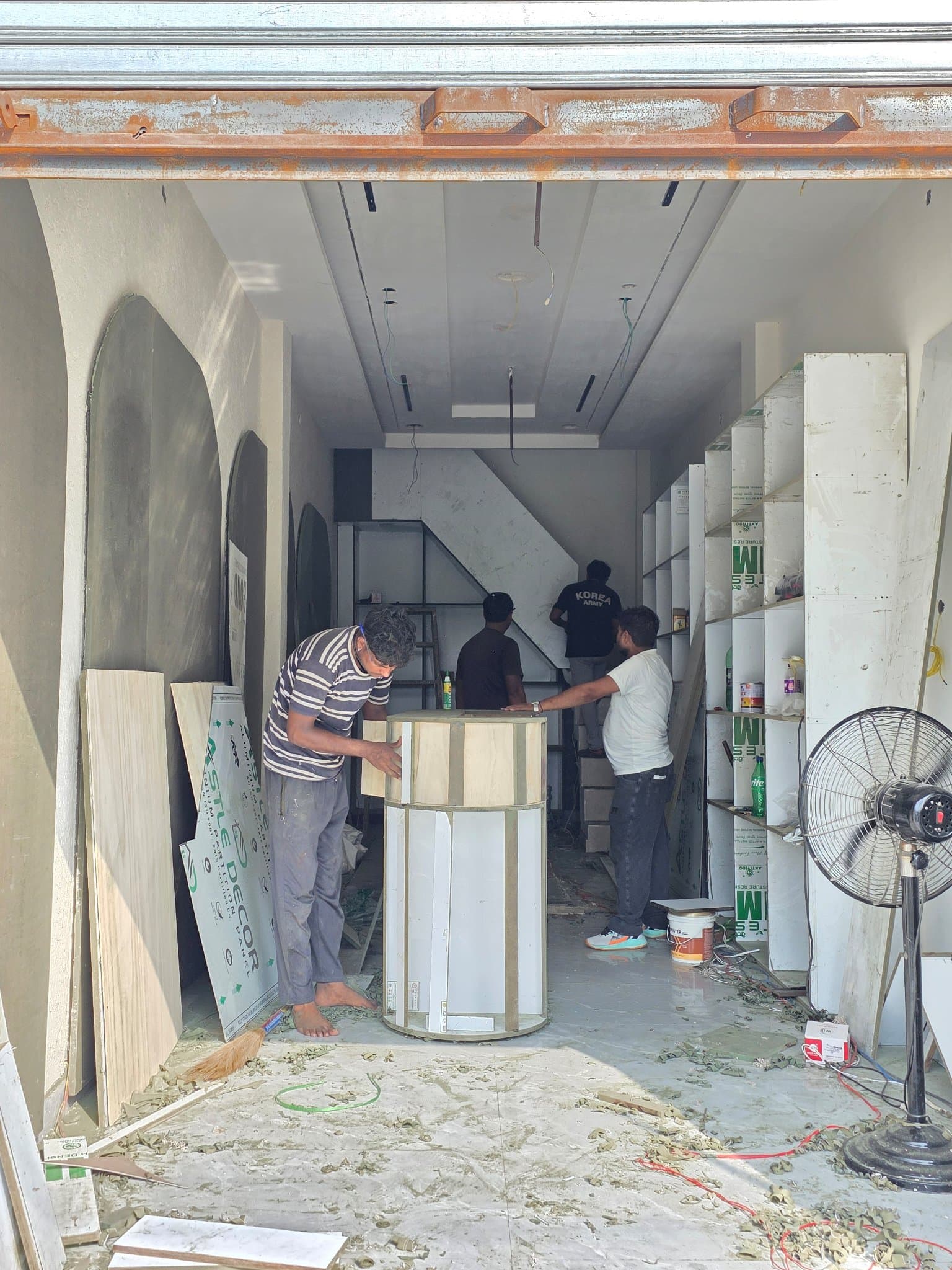 Three construction workers assembling a custom circular wooden display counter inside a partially finished retail shop space.
